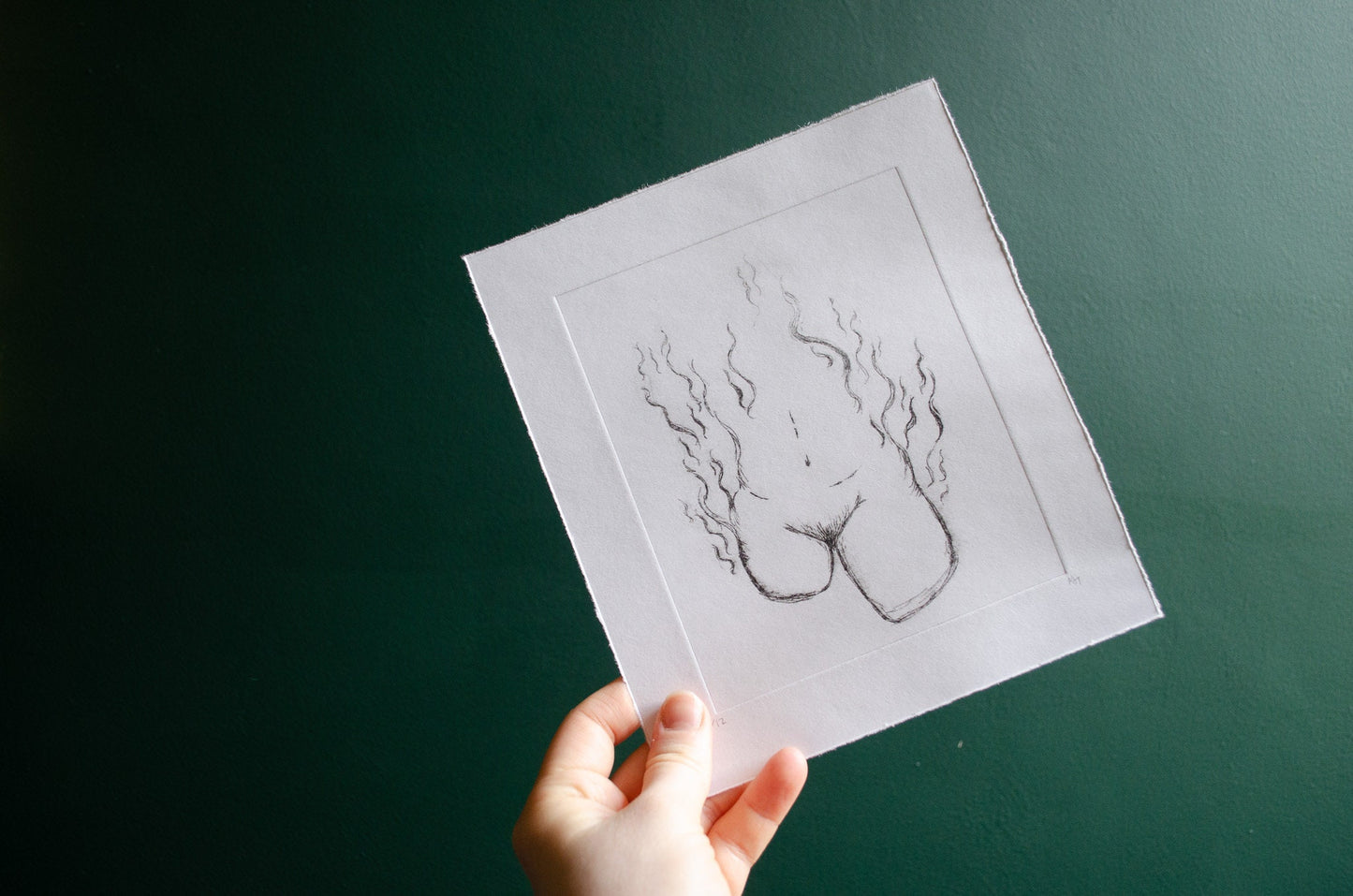 Hand holding a dry point etching of an abstract female nude in front of a green wall
