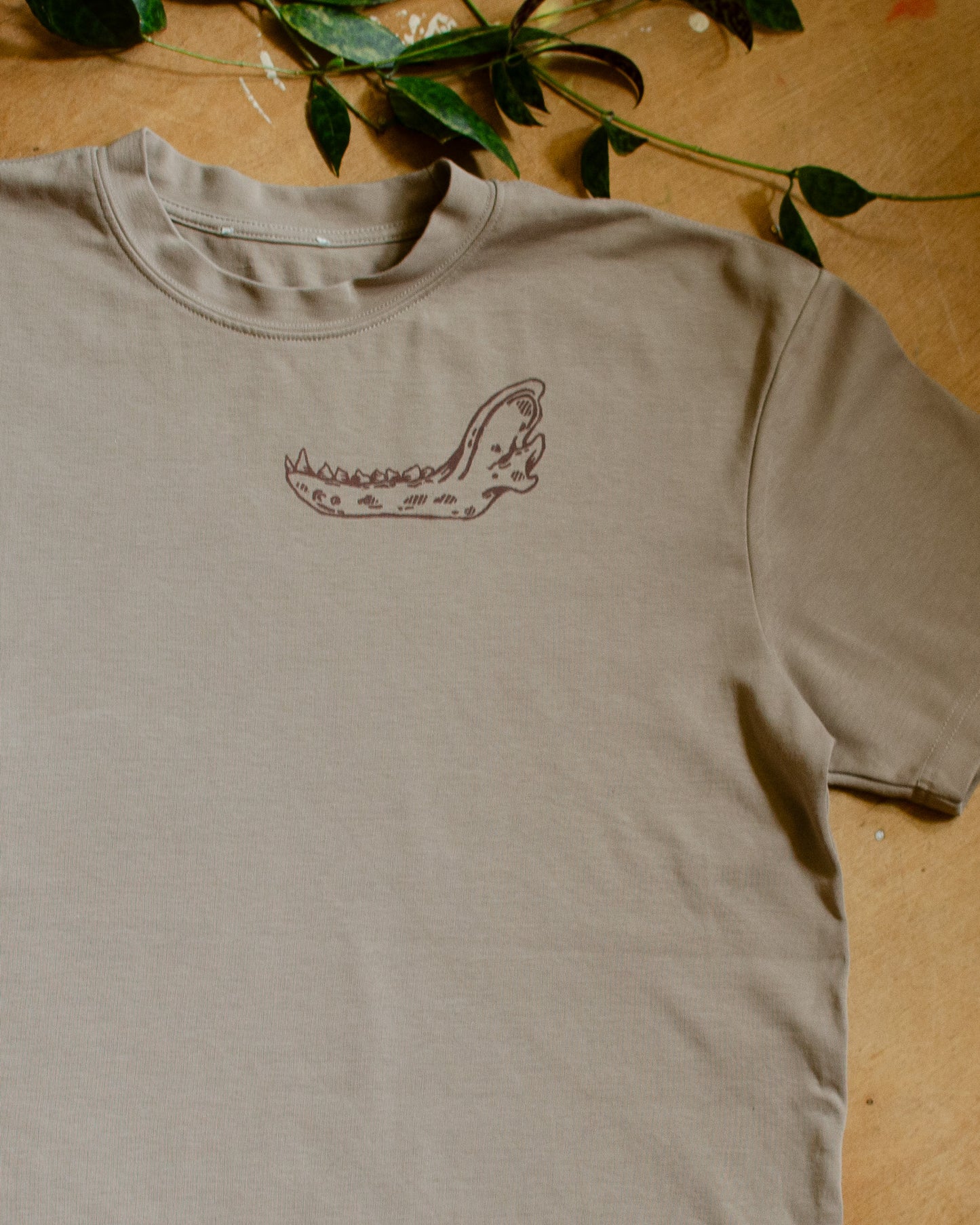 Beige t-shirt with an animal jawbone print on a wooden surface with green leaves.