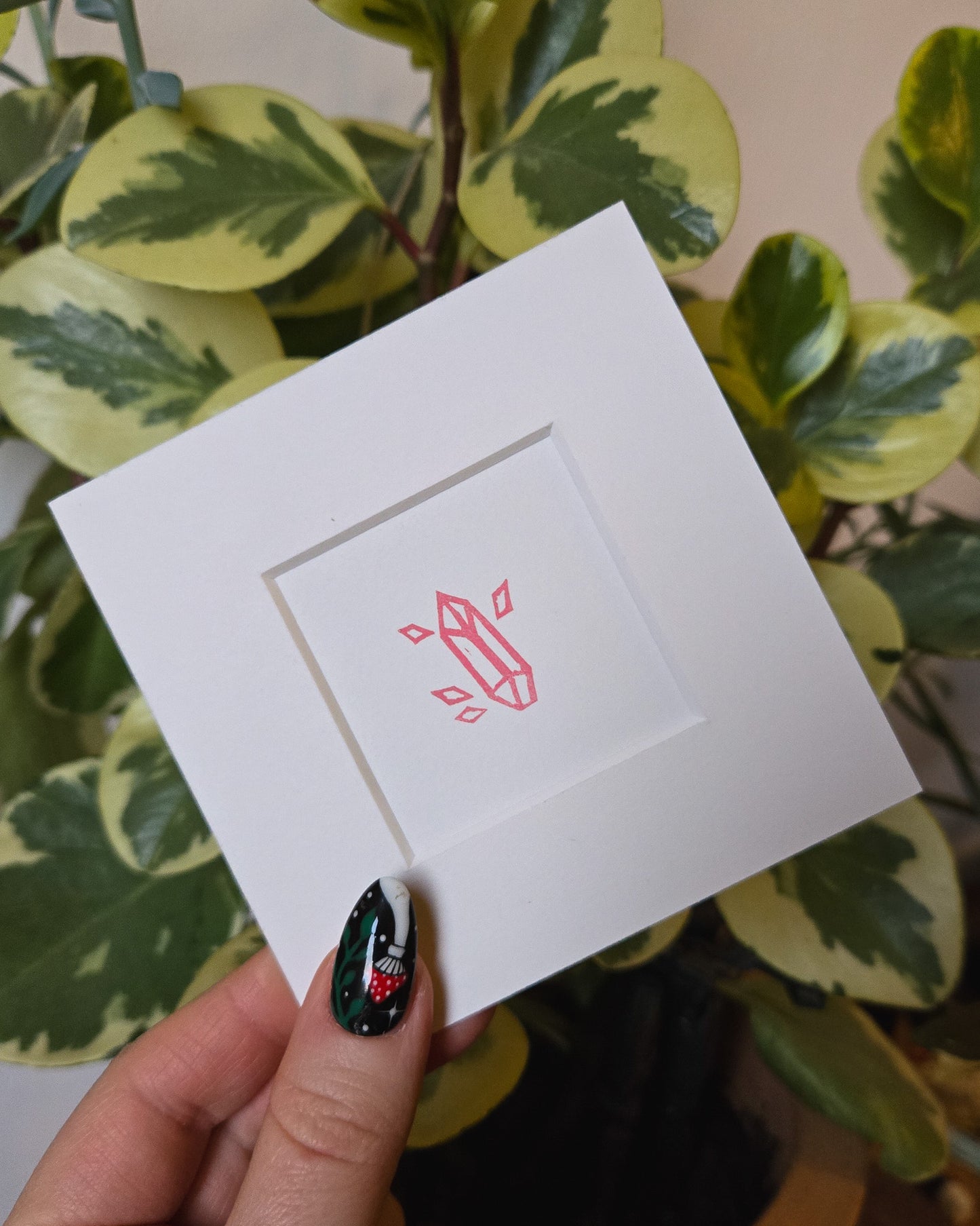 White card with pink crystal design held by a hand against a green leafy background