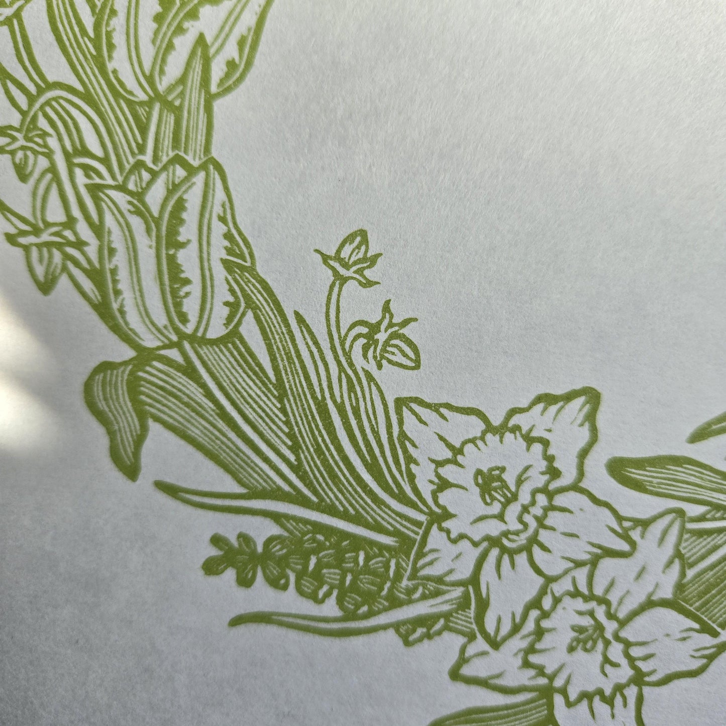 Close up of a linocut print of a spring floral wreath in light green ink on white paper
