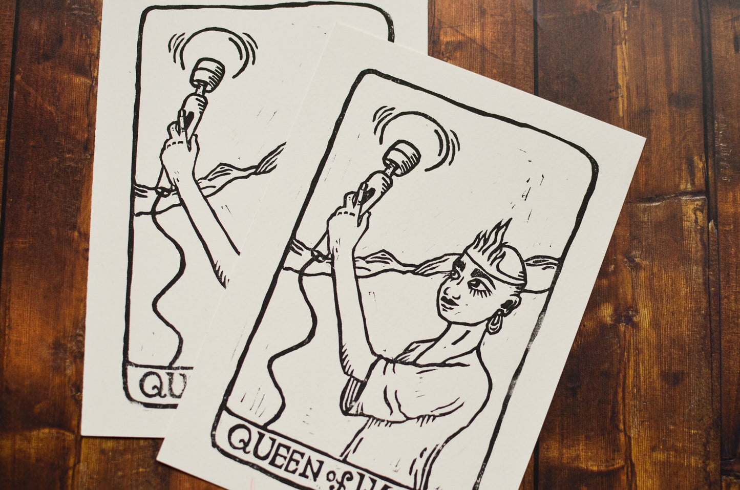 Black and white linocut print of a tarot card of the Queen of Wands on a wooden surface