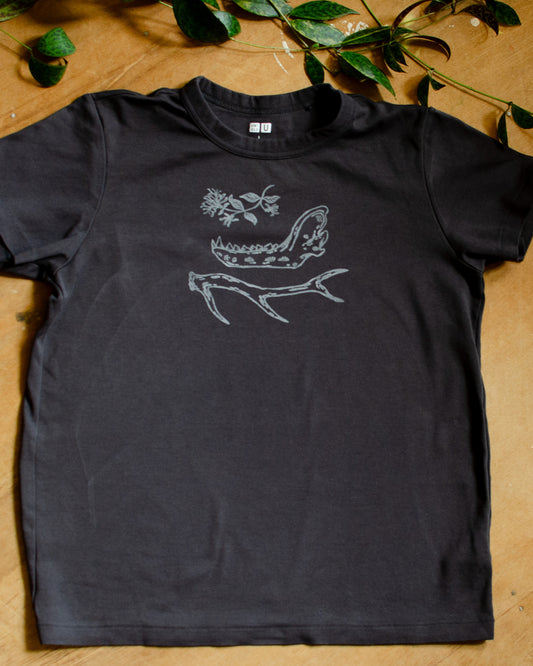 Black t-shirt with hand printed white honeysuckle, jawbone, and antler design on a wooden surface with green leaves.