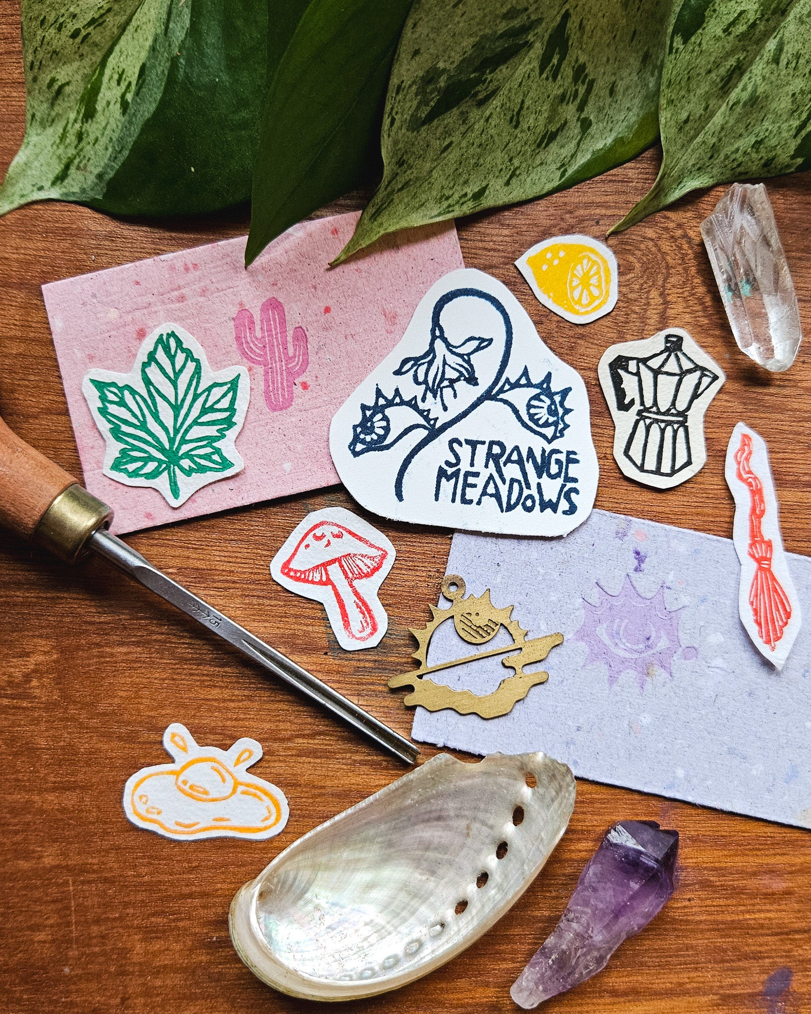 Collection of cut out mini linocut prints and Strange Meadows business cards on a wood surface