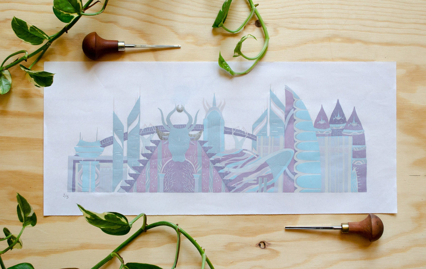 Linocut print of a pastel hued sci-fi city skyline sitting on a wooden surface