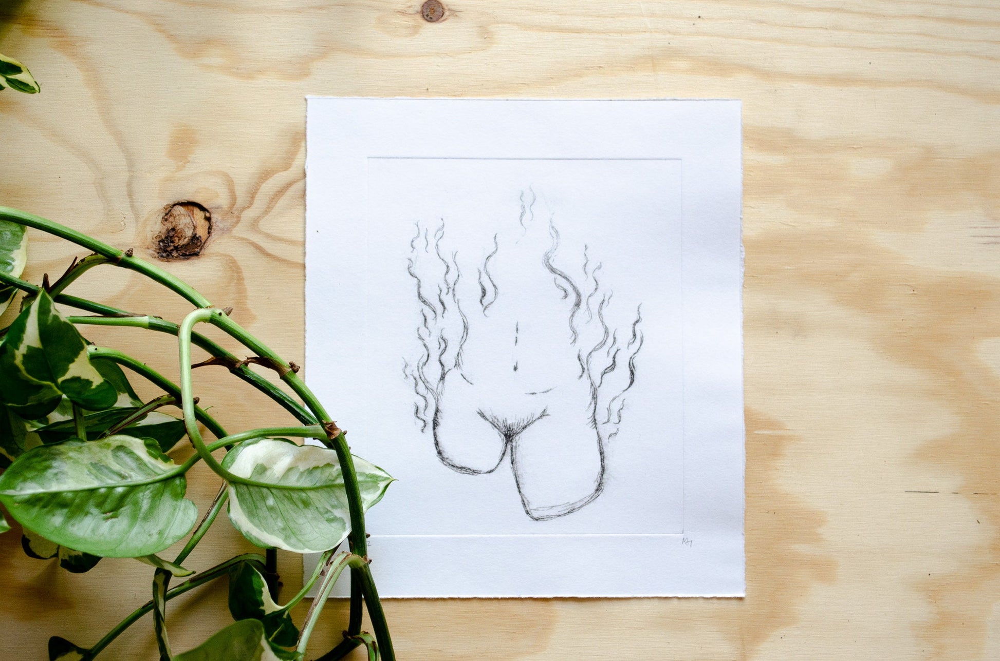 A dry point etching of an abstract female form sits on a wooden table