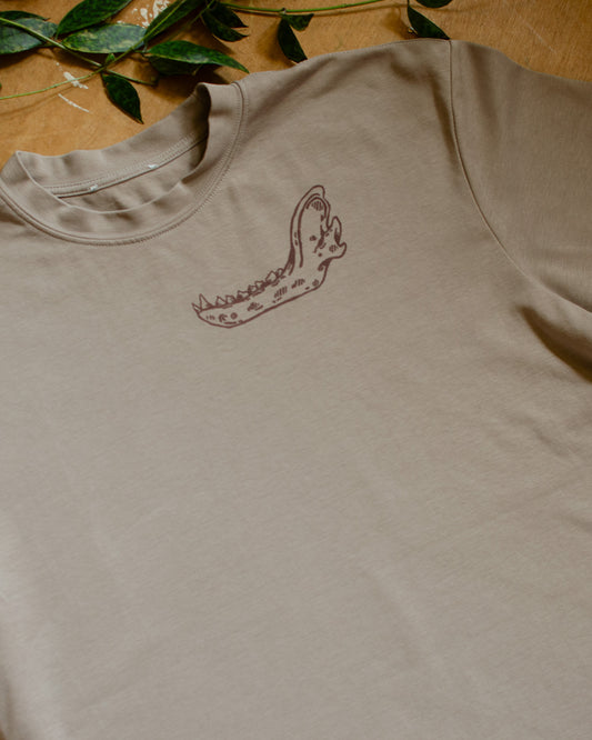 Beige t-shirt with an animal jawbone print on a wooden surface with green leaves.
