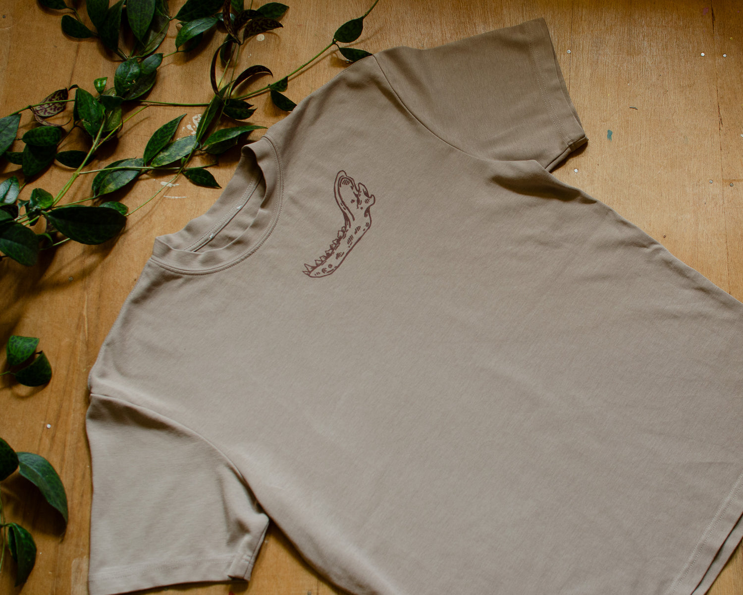 Beige t-shirt with an animal jawbone print on a wooden surface with green leaves.