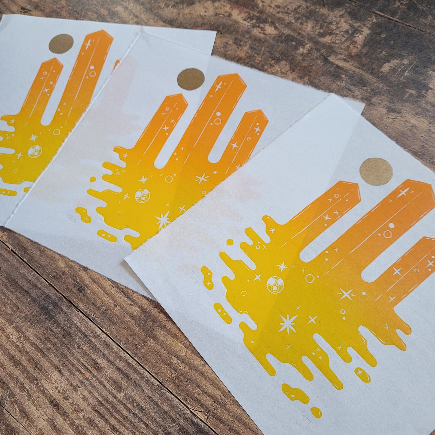 Three sheets of paper with yellow and orange skyscrapers designs on a wooden surface