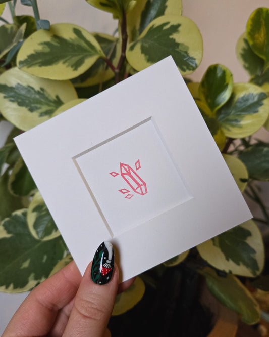 White card with pink crystal design held by a hand against a green leafy background