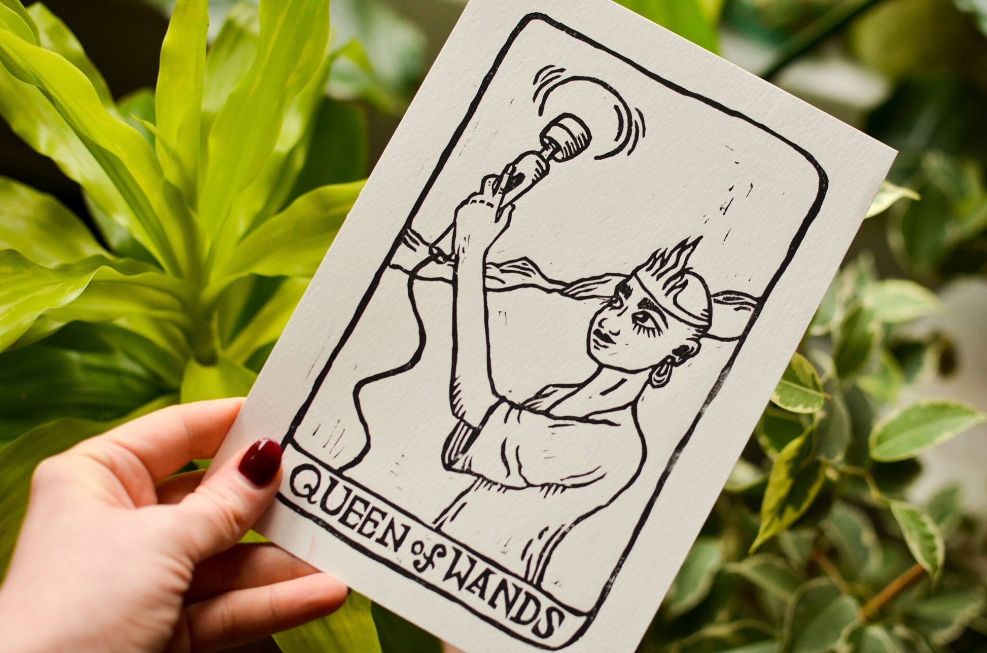 Card featuring 'Queen of Wands' with a hand holding it against a leafy background