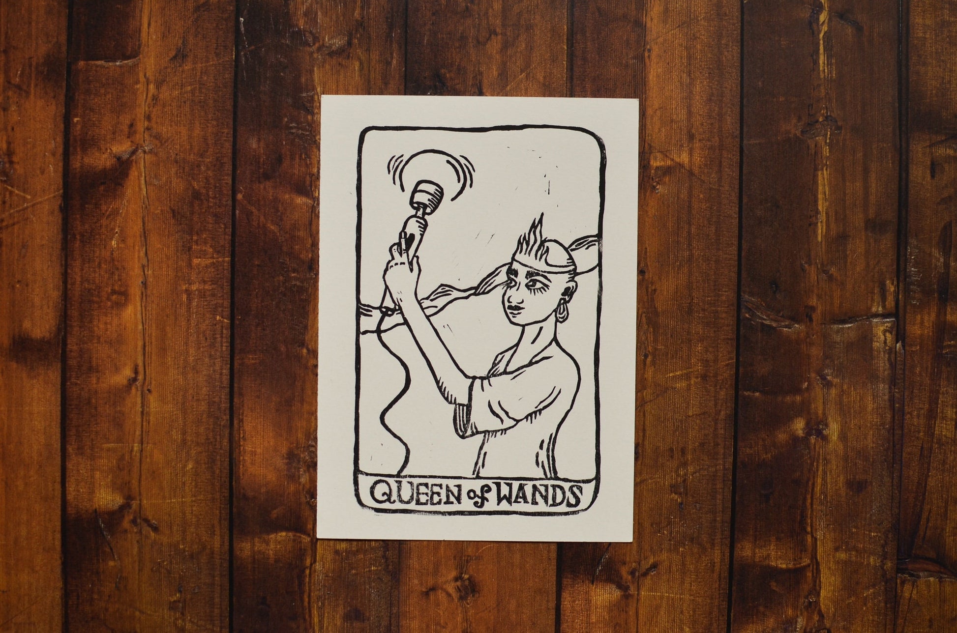 Black and white linocut print of a tarot card of the Queen of Wands on a wooden surface