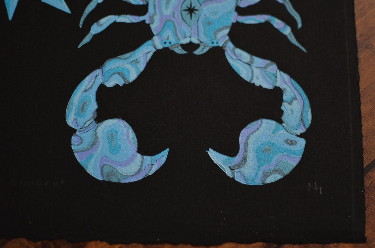 Close up of a blue linocut print of a scorpion, on black paper focusing on the claws and eyes