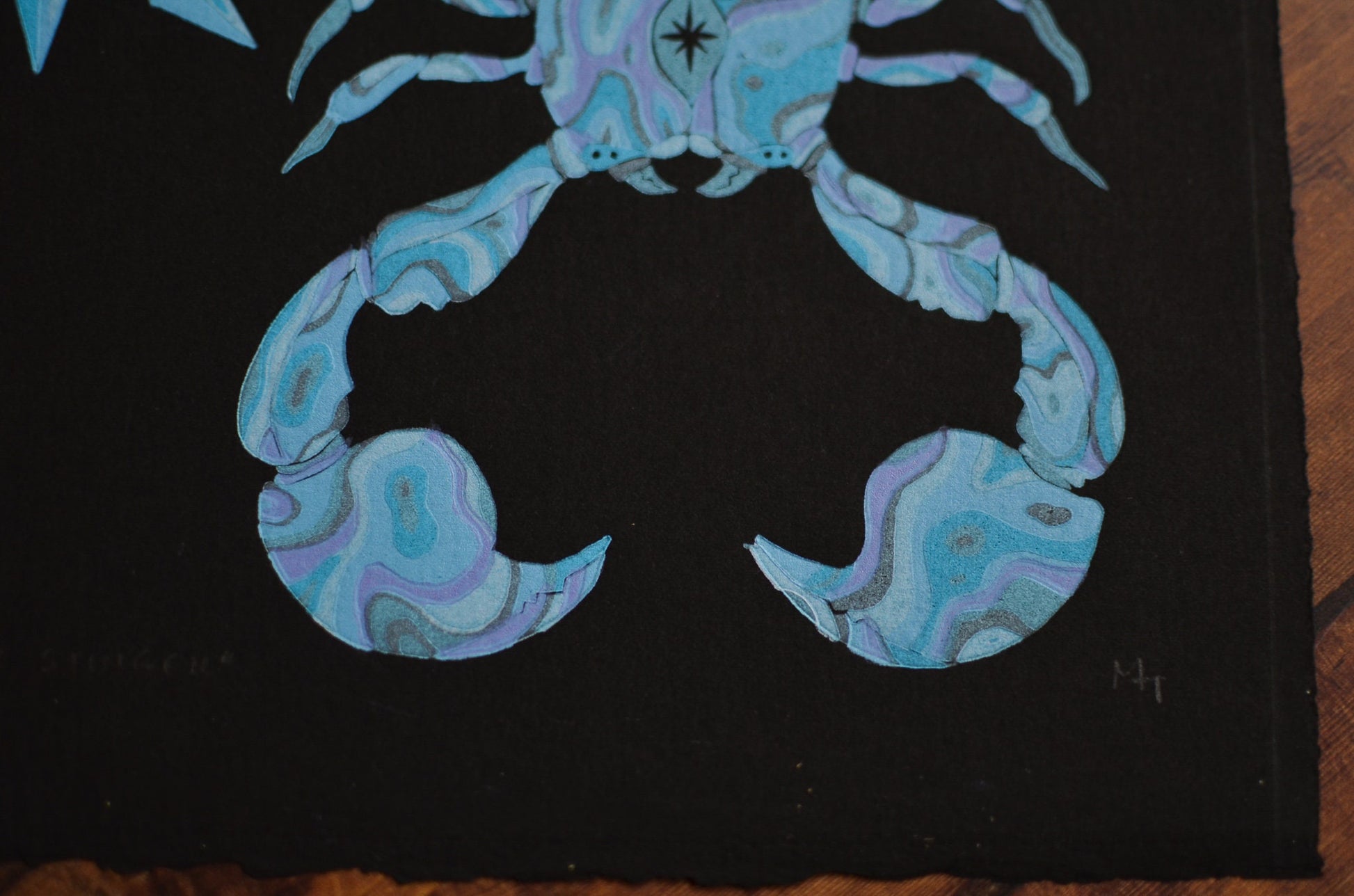Close up of a blue linocut print of a scorpion, on black paper focusing on the claws and eyes