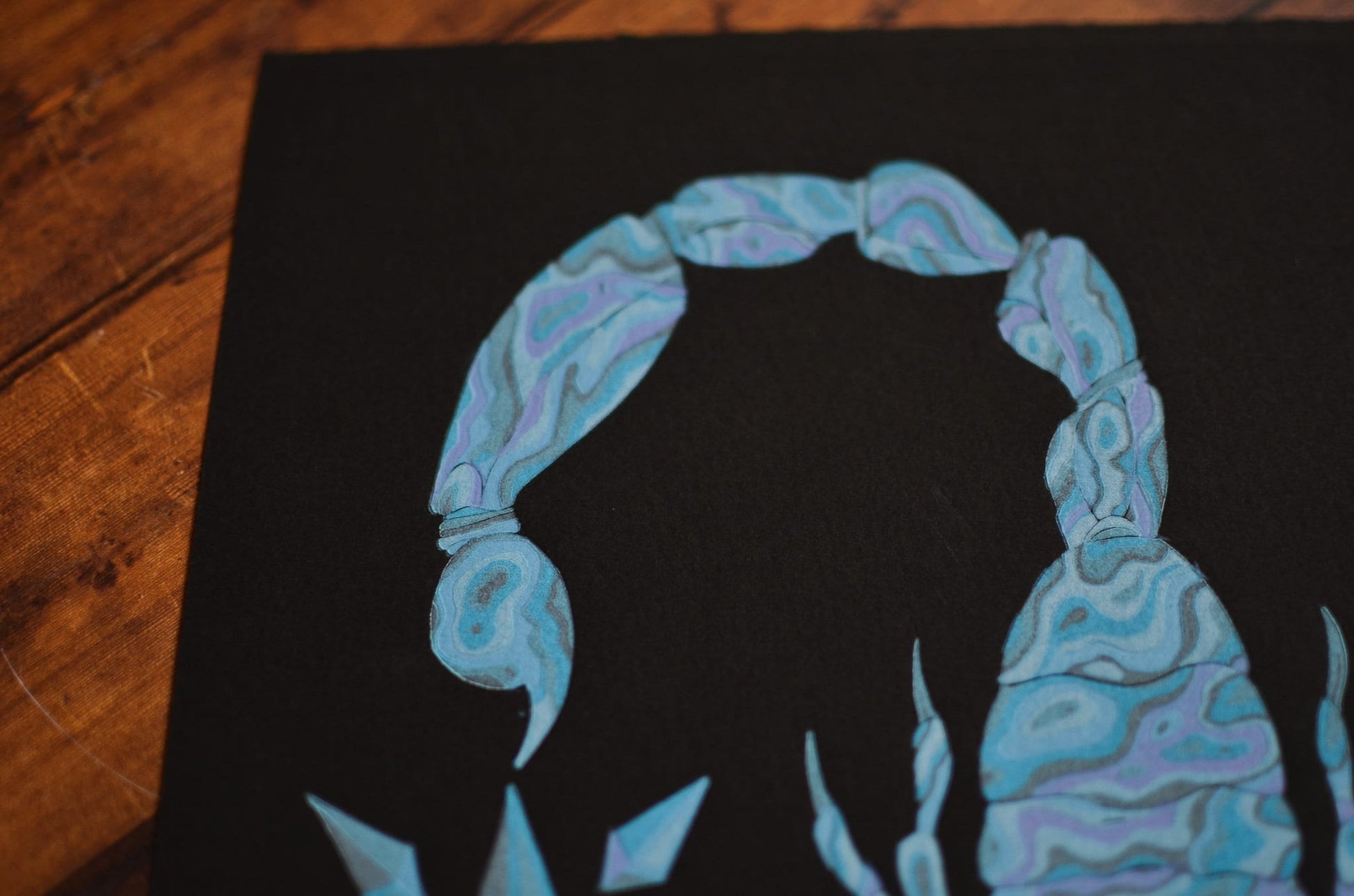 Close up of a blue linocut print of a scorpion, on black paper focusing on the tail