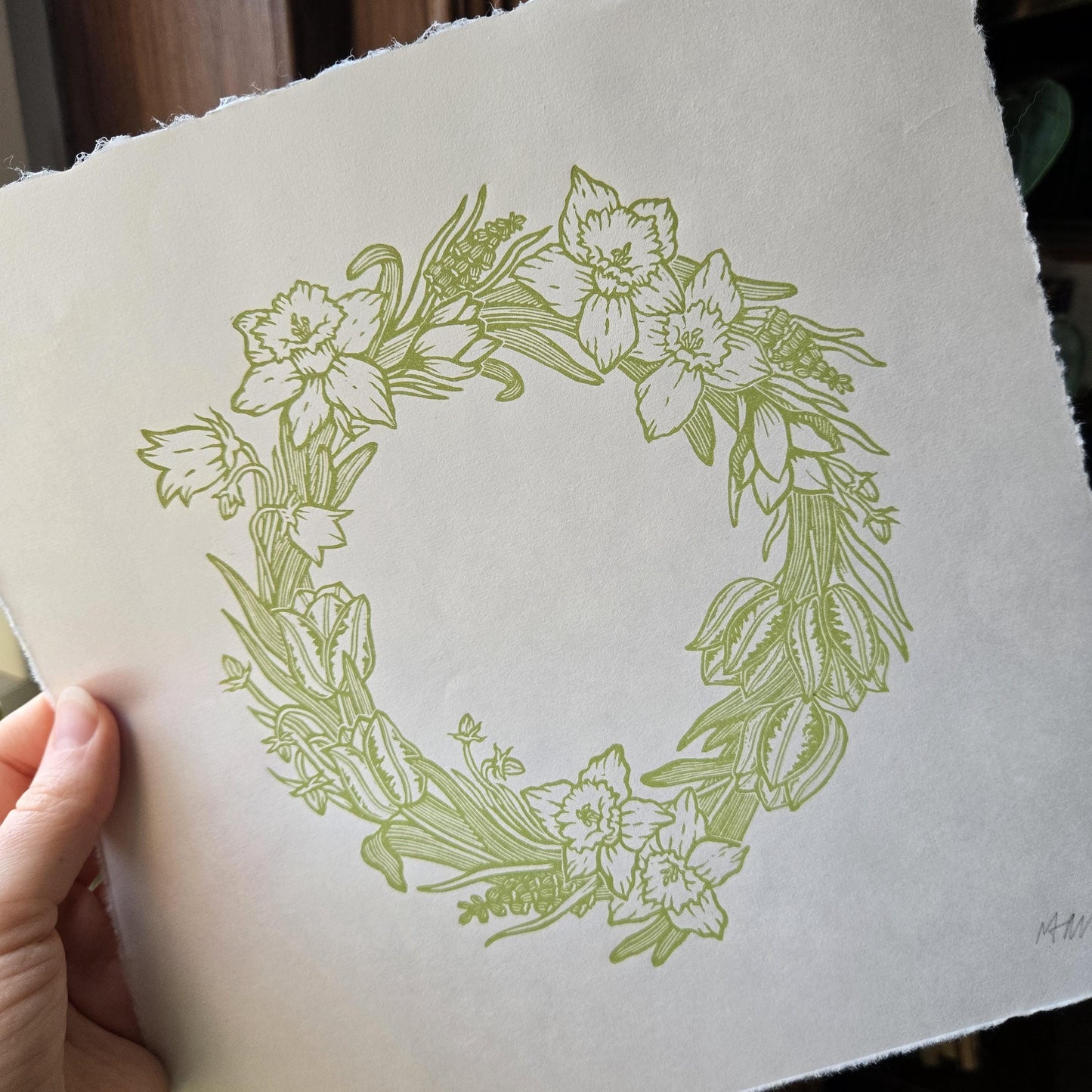 Floral wreath linocut print on a white background held by a hand
