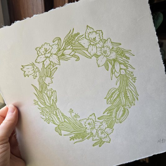 Floral wreath linocut print on a white background held by a hand