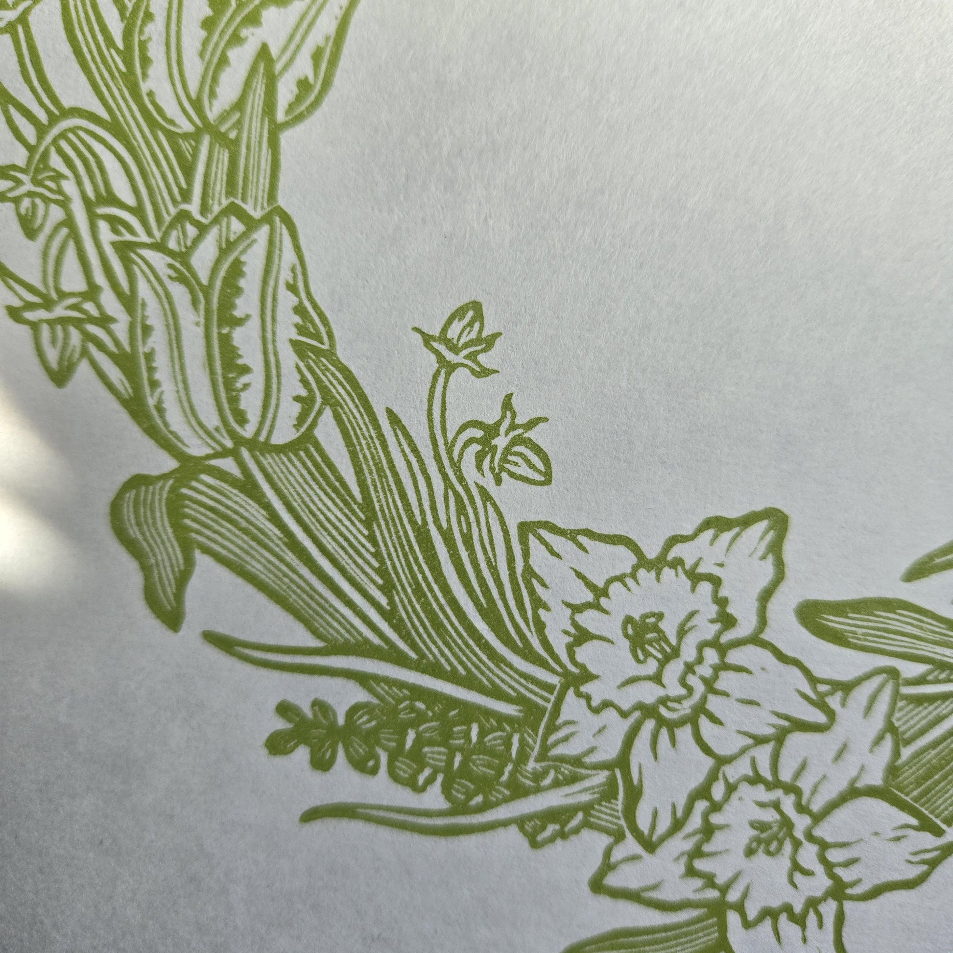 Close up of a linocut print of a spring floral wreath in light green ink on white paper