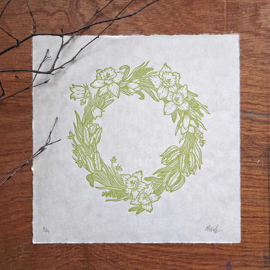 Floral wreath design on a white sheet of paper with branches on a wooden surface