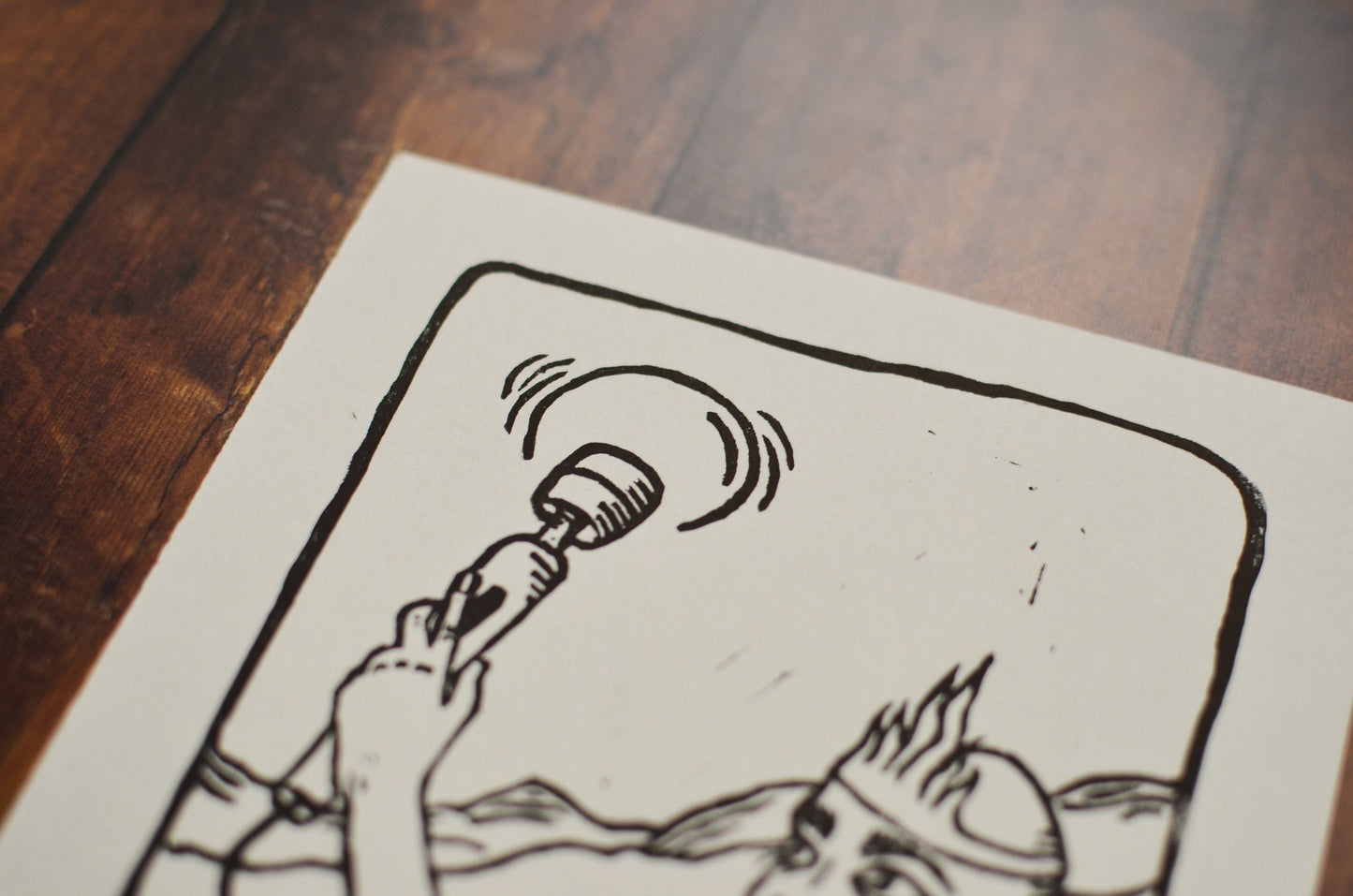 Close up of a black and white linocut print of a tarot card of the Queen of Wands on a wooden surface