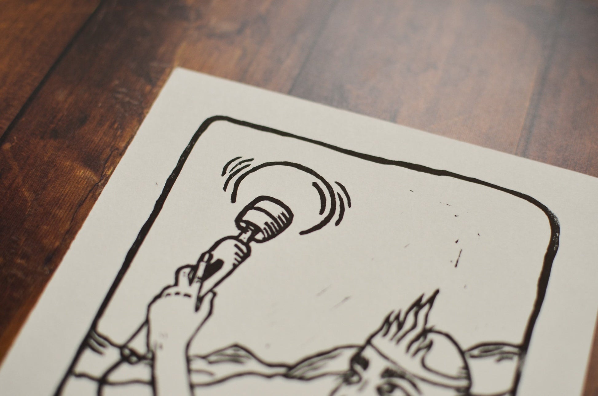 Close up of a black and white linocut print of a tarot card of the Queen of Wands on a wooden surface