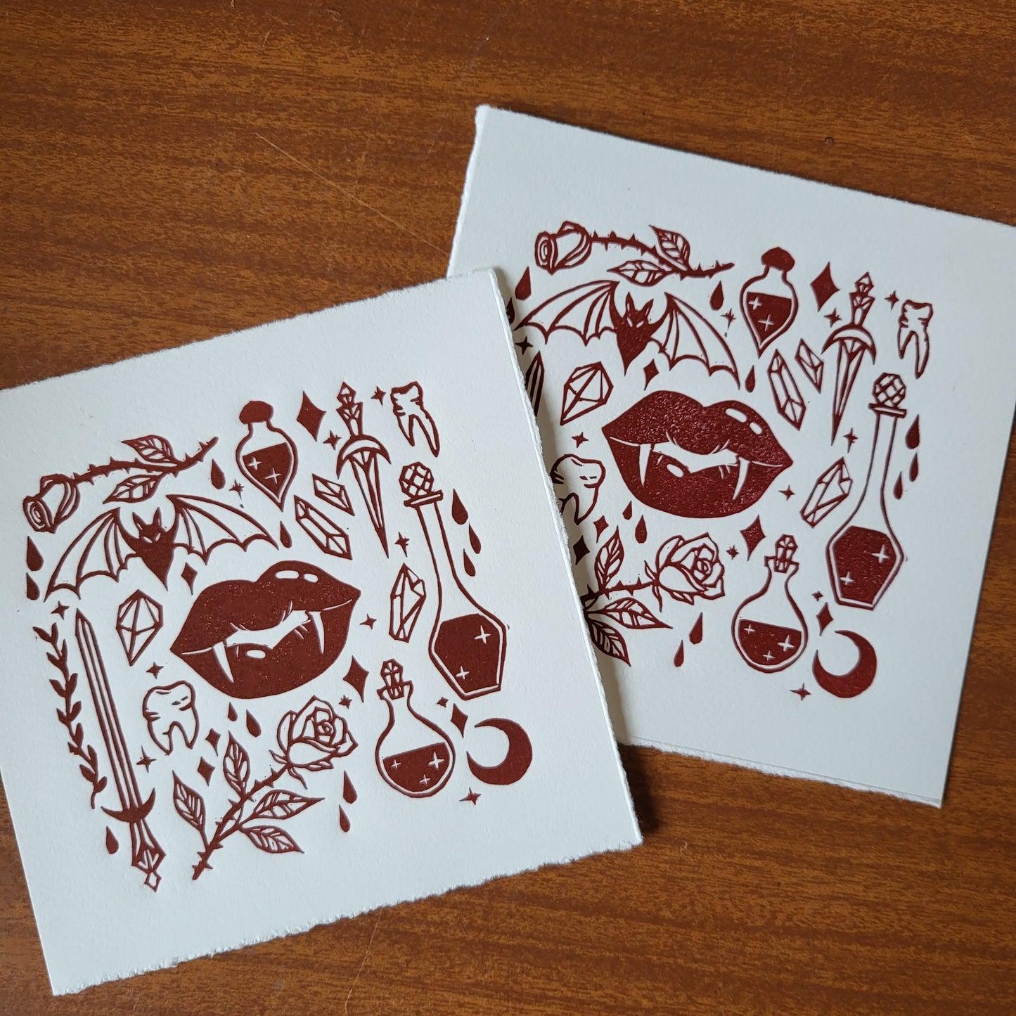 Two sheets of paper with red tattoo style vampire witch designs on a wooden surface
