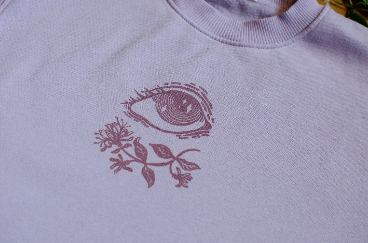 Light violet sweatshirt with a pink floral and eye design.